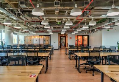 Large open-plan office space featuring rows of wooden desks under industrial ceilings and pendant lighting.