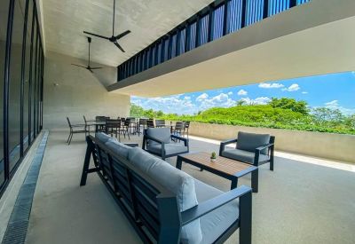 Spacious covered balcony lounge with modern grey sofas and a view of green trees.