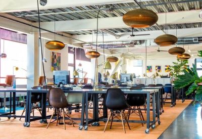 Bright coworking space with long shared tables, ergonomic chairs, and large windows.