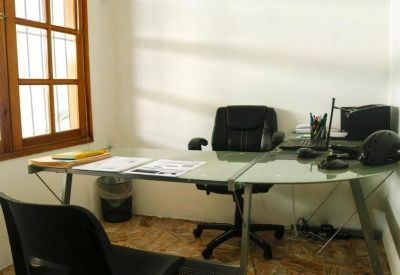 Small private office featuring an L-shaped glass desk and wooden window frame.