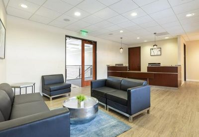 Bright reception area with dark leather seating, wooden desk, and a blue rug.