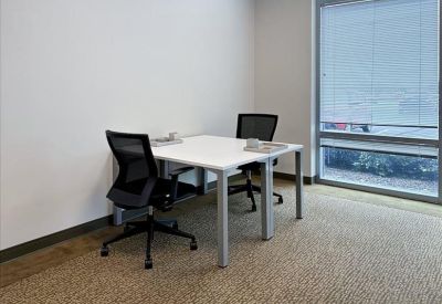 Bright private office suite with two black mesh chairs and a white desk by a large window.