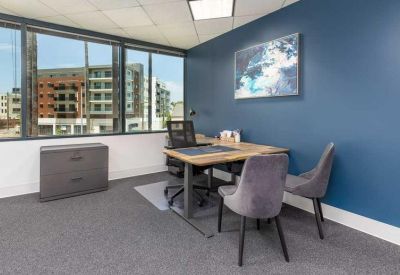 Private office suite with a wooden desk, plush grey guest chairs, and a blue accent wall.