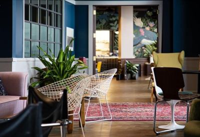 Vibrant workspace entrance with a pink sofa, indoor plants, and a colorful patterned rug.