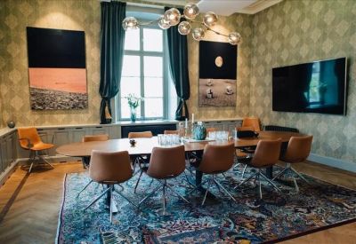 Elegant meeting room with a long wooden table, leather chairs, and contemporary art on patterned wallpaper.