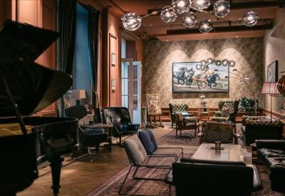 Moody lounge area featuring a grand piano, leather armchairs, and a gallery wall under warm orb lighting.