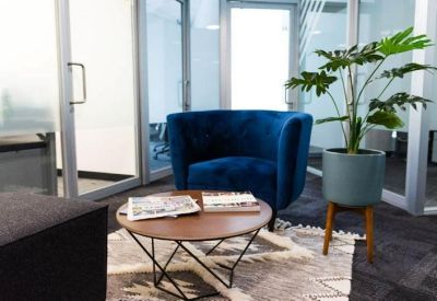 Lounge area featuring a plush blue armchair, round wooden coffee table, and a potted plant.