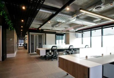 Open-plan office with white desks, ergonomic chairs, and industrial exposed ceilings.