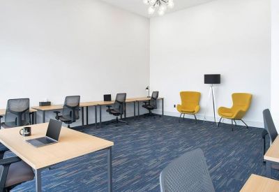 Spacious coworking area with long wooden desks, ergonomic chairs, and bright yellow accent armchairs.