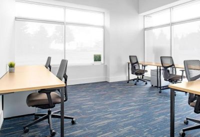 Open-plan office space with multiple workstations near large windows providing ample natural light.