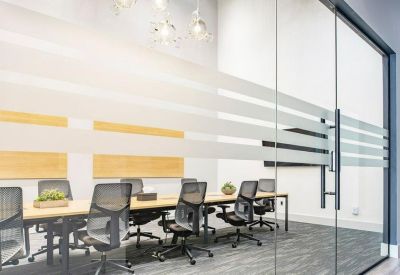 Glass-walled conference room with a long table, mesh chairs, and frosted privacy banding.