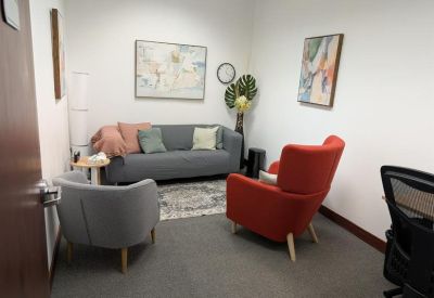 Lounge area with a grey sofa, red armchair, and colorful wall art.