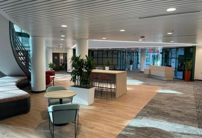 Modern building lobby with a curved staircase, seating area, and indoor plants.
