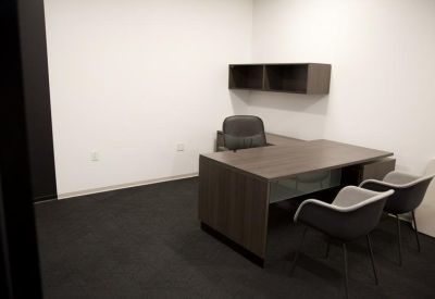 Private office with a dark wood desk and two grey guest chairs.
