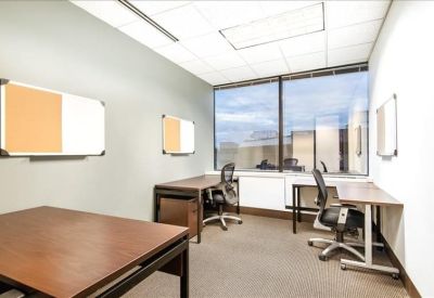 Private office suite featuring three wooden desks and natural light from a large window.