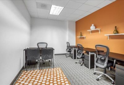 Bright multi-desk office workspace with an orange accent wall and patterned rug.