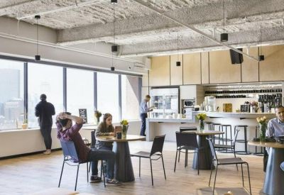 Modern communal kitchen and cafe area with industrial ceilings and city views.
