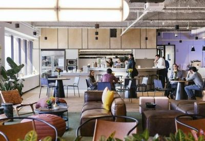 Spacious breakout lounge with leather sofas, plants, and a service bar in the background.