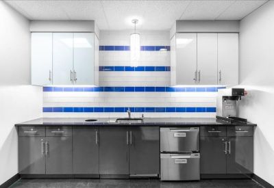 Modern breakroom kitchen featuring dark cabinetry and a blue striped tile backsplash.