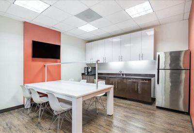 Modern communal kitchen area with white cabinetry, stainless steel fridge, and dining table.