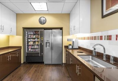 Office kitchen with a vending machine, large refrigerator, and dark wood cabinetry.