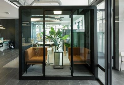 Modern interior at 100, King Street West featuring a glass meeting pod with tan seating and a large indoor plant.