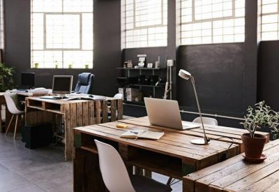 Open-plan workspace with rustic wooden pallet desks and white chairs near large industrial windows.