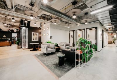 Modern lounge area with grey armchairs, potted plants, and industrial-style ceiling.