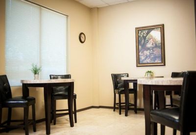 Communal break area with small round tables, black cushioned chairs, and framed wall art.