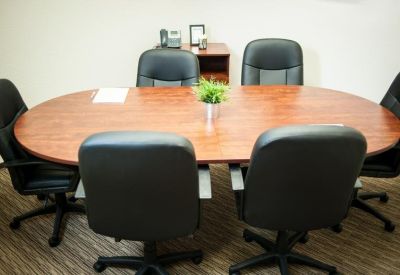 Small meeting room with an oval wooden table and five black leather office chairs.