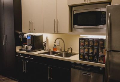 Modern kitchen and break area with dark cabinetry, stainless steel appliances, and coffee station.