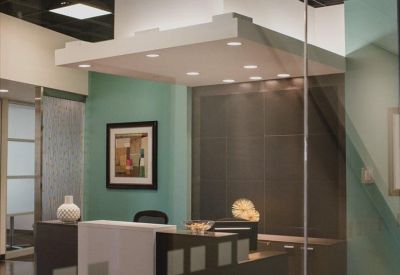 Reception area with a dark wood desk, teal feature wall, and illuminated architectural ceiling.