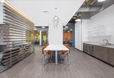 Communal break area with a white dining table, modern kitchenette, and slatted wood room divider.