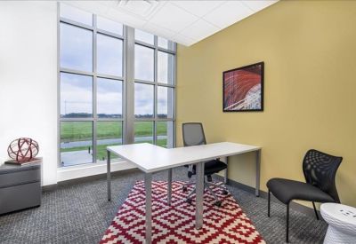 Private office featuring a large window, L-shaped white desk, and a red patterned rug.