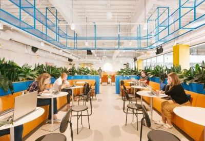Vibrant coworking space with orange booths, indoor plants, and blue architectural accents.