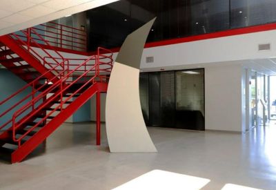Spacious lobby area with polished floors, red metal railings, and a minimalist white sculpture.