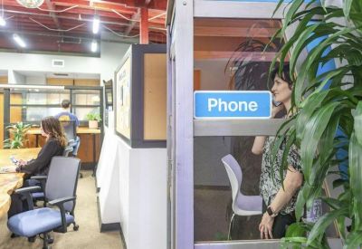 Internal office corridor featuring a private phone booth and indoor greenery.