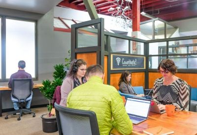 Collaborative office area with glass-partitioned workspaces and people using laptops.