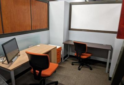 Small meeting room or private office with two desks, orange chairs, and a whiteboard.