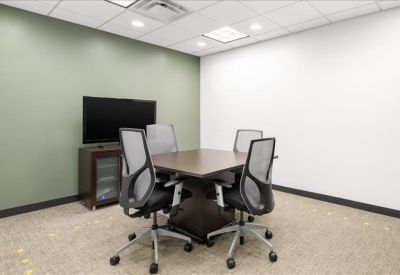 Small meeting room with a dark wood table, four grey chairs, and a television.