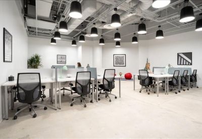 Spacious coworking area with white desks, ergonomic chairs, and industrial ceiling lighting.