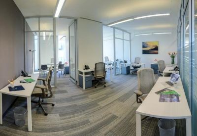 Glass-walled private office suite with white desks and minimalist grey flooring.