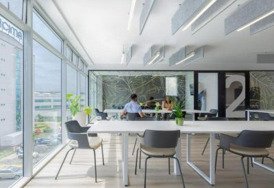 Bright coworking area with white desks, indoor plants, and floor-to-ceiling windows.