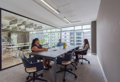 Modern glass-walled meeting room with a long table and views of surrounding city buildings.