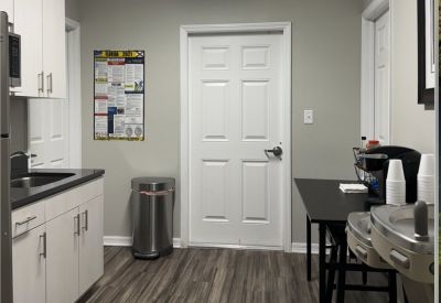 Office kitchen area with white cabinetry, coffee station, and high-top dining table.