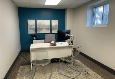 Private office suite with a white desk, teal accent wall, and three-panel wall art.