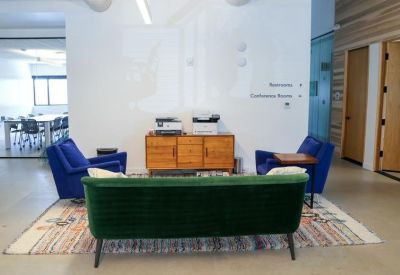 Breakout area with a green velvet sofa, blue chairs, and a wooden sideboard.