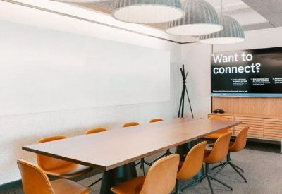 Modern conference room with a long wooden table, orange chairs, and a large wall-mounted screen.