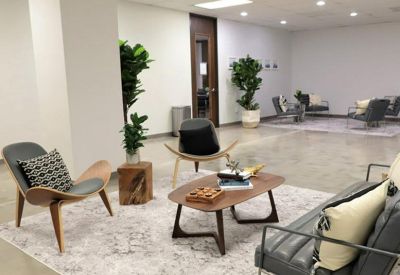 Spacious communal lounge with mid-century modern chairs, potted plants, and a wooden coffee table on a patterned rug.