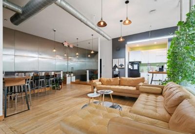 Bright communal lounge with tan leather sofas, wooden floors, and hanging pendant lights.